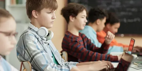 School children sitting at their desks with a laptop in front of them