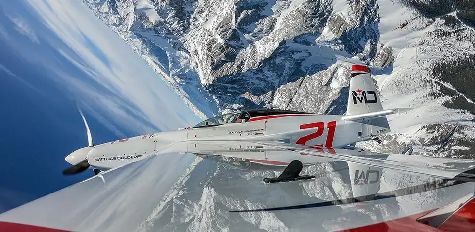 Blick auf ein sich auf den Kopf drehendes Sportflugzeug über schneebedeckte Berge