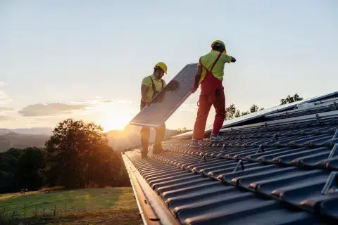 Image where two men are installing solar panels on a roof during sunset.