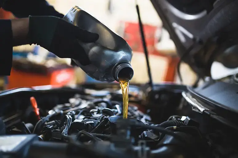 close up hands of mechanic pouring engine oil into a car