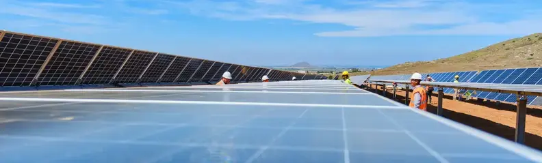 Personas con casco y chalecos reflectantes naranjas trabajando en torno a una placa fotovoltaica