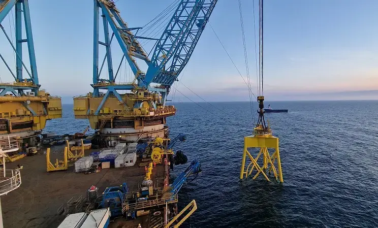 Yellow foundation for offshore wind turbine being lifted into the sea by large crane