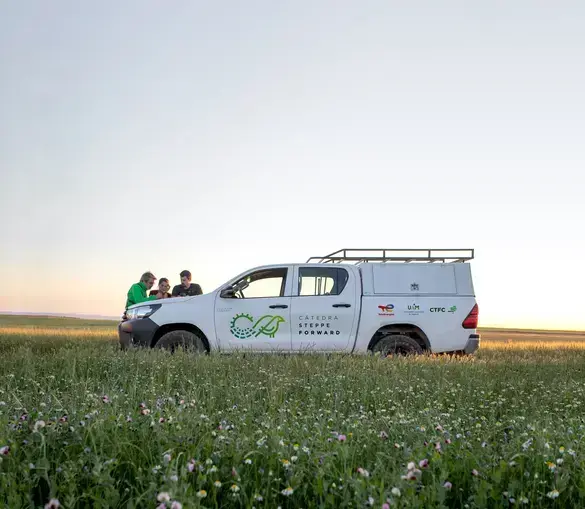 Tres personas consultan algo sobre el capó de una furgoneta en medio del campo