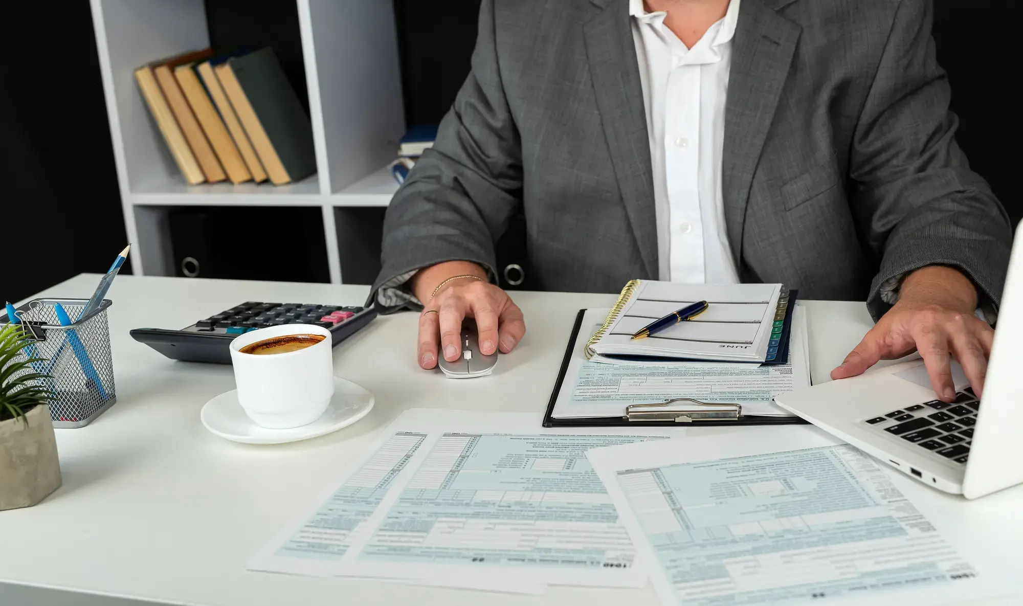 An image of a person walking on a laptop at a desk, surrounded by paper and pens.