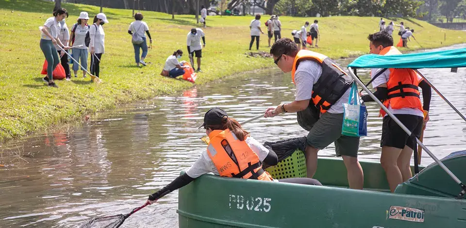 employees on a power boat picking up litter while others picking up litter on foot