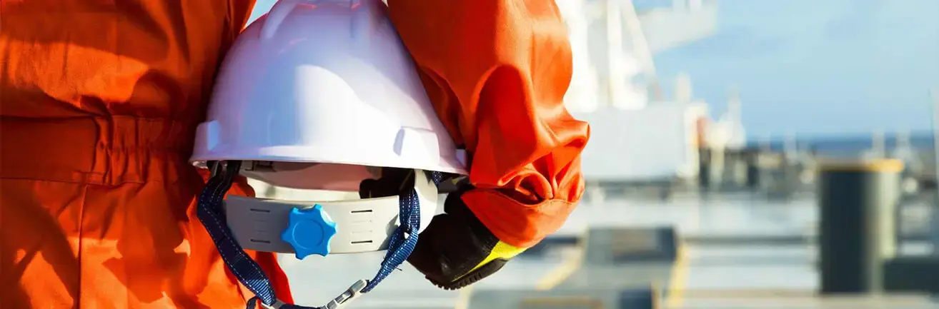 Detail pracovníka v oranžové kombinéze, který u boku drží bílou helmu