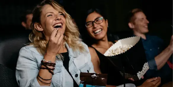 Two women and a man sitting in the cinema eating popcorn