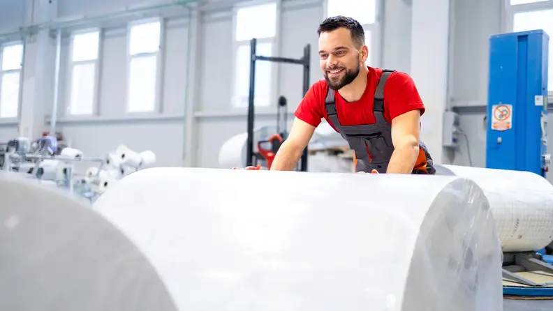 Trabajador operando maquinaria de papel en planta.