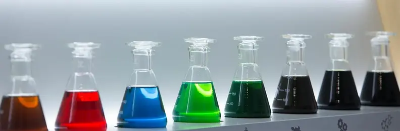 Messbecher mit unterschiedlich farbigen Motorölen auf einem weißen Podest.