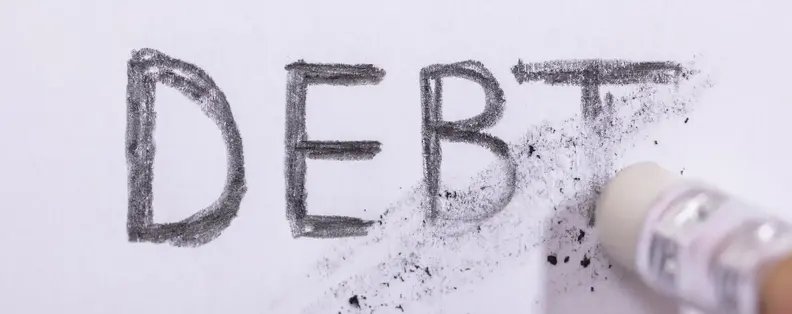 An image of the word Debt in Pencil, being erased by an eraser.