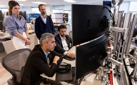 three workers looking at a computer screen on the trading floor