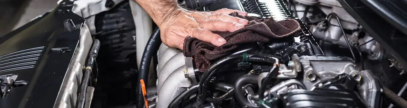 Männerhand wischt mit einem Lappen über einen Automotor