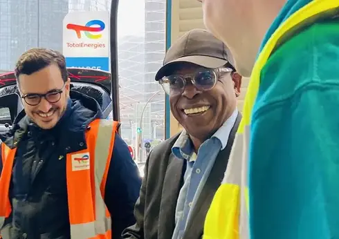 3 Menschen im Gespraech in einer Stadt mit TotalEnergies Logo im Hintergrund 