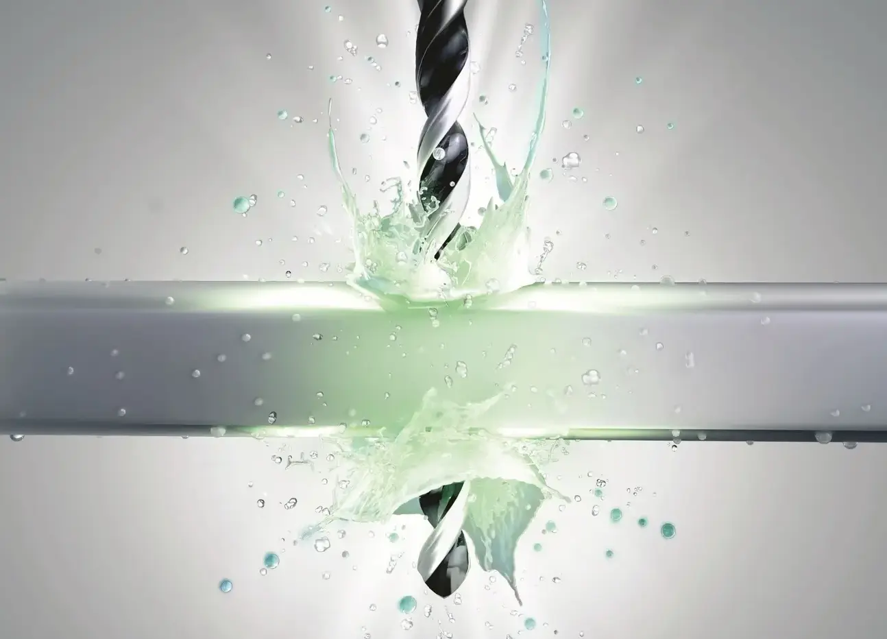 drill bit cutting through metal with cooling fluid splash